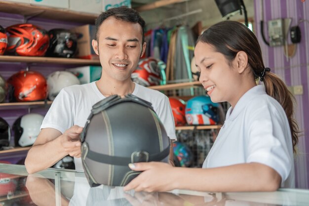 Male and female shop assistants holding a helmet against a helmet display rack in a helmet shop