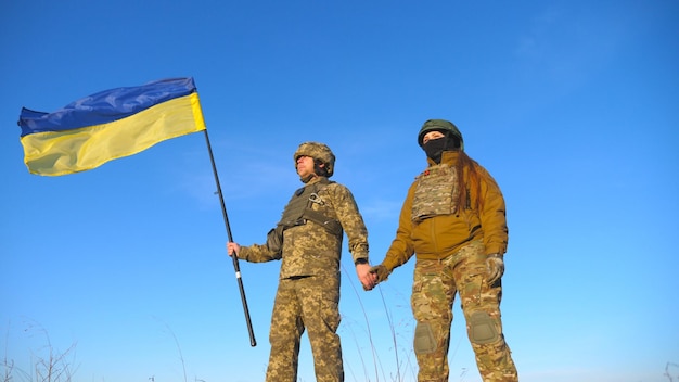 Male and female ukrainian army soldiers holding hands of each other and lifted up flag against blue sky military people waving flag of ukraine in honor of the victory against russian aggression