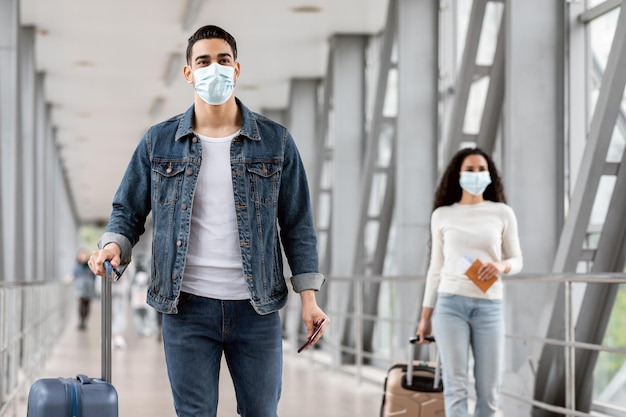 Male and female wearing face masks while walking with luggage at airport