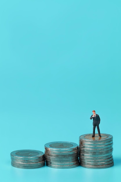 Male figurine on stack of coins against blue background