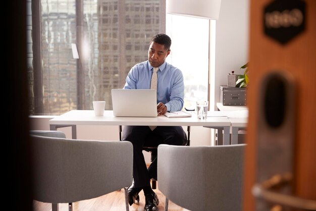 Финансовый консультант-мужчина в современном офисе сидит за столом и работает на ноутбуке