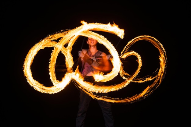 Male fire dancer twirl burning baton creating sparkling trails in motion dark outdoors twirler