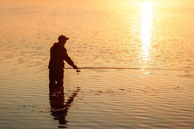 Foto il pescatore maschio all'alba sul lago pesca una canna da pesca vacanza di hobby di pesca