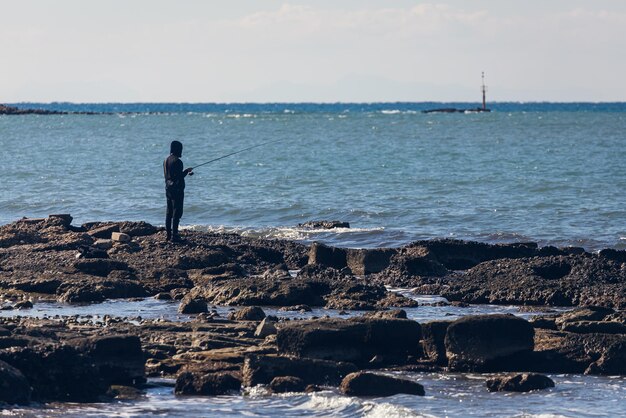 黒いレインコートを着た男性の漁師が冬の海で魚を捕まえる