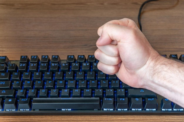 male fist with force hits the keyboard with the backlight, lying on the table