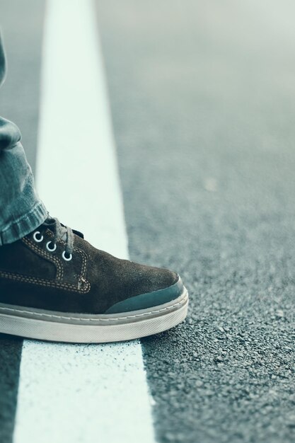 흰색 선에 서 있는 남성 발. 교차 선 개념입니다. 아스팔트 도로에 남성 신발입니다. 경계선 개념입니다.