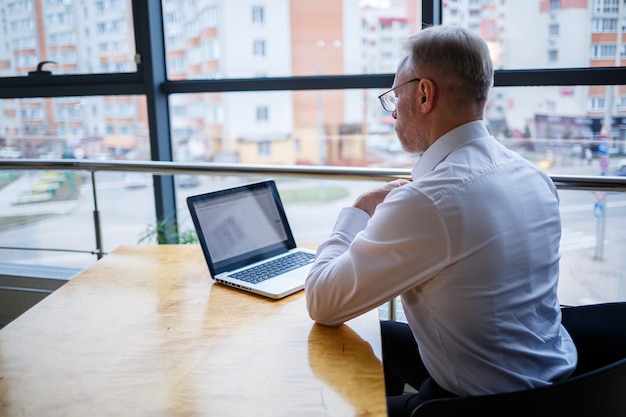 Male freelancer is working in a cafe on a new business project. sits at a large window at the table. looks at a laptop screen with a cup of coffee