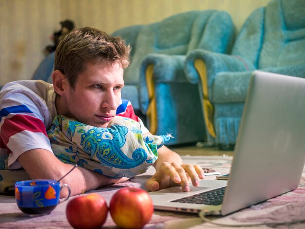 Male freelancer lying in front of laptop at home working