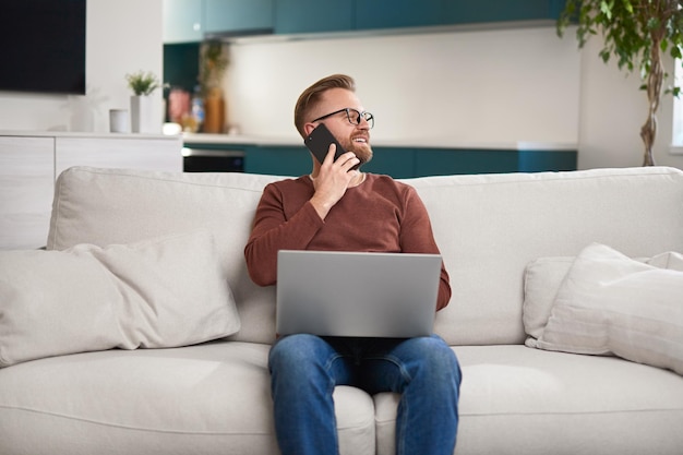 Male freelancer with laptop speaking on smartphone