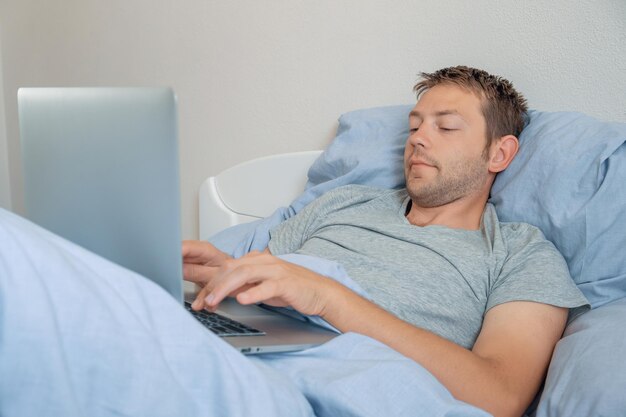 Male freelancer working with laptop in bed in the morning man designer on remote work from home