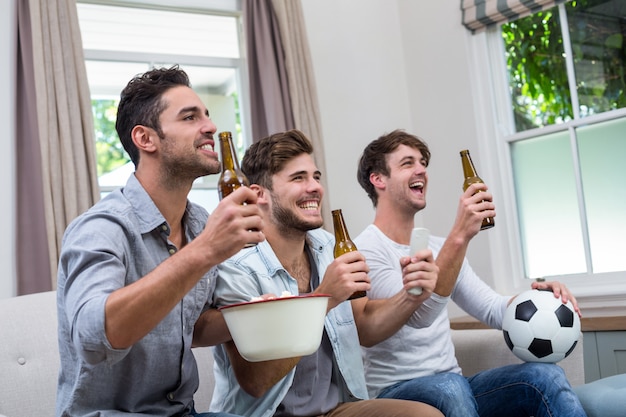 Male friends enjoying beer while watching soccer match on TV