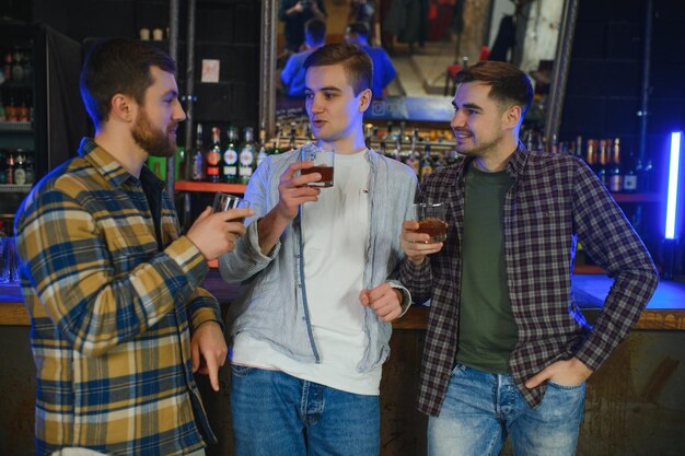Male friends spending time together in bar and having fun Bearded men smiling looking at each other and communicating Men holding crystal glasses of whisky or scotch