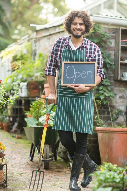 Male gardener with open sign holding gardening fork