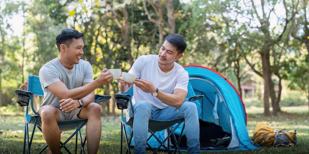 Male gay couple asian traveling with tent camping outdoor and various adventure lifestyle hiking active summer vacation drinking coffee and talking together