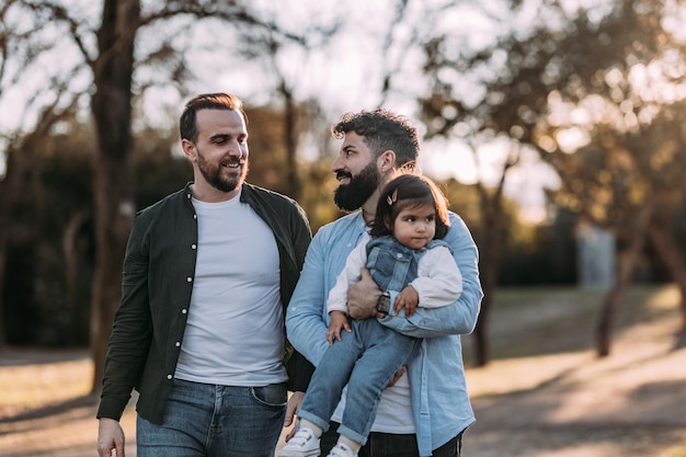 写真 男性の同性愛者のカップルは彼らの腕の中で彼らの娘と恋に公園を歩く