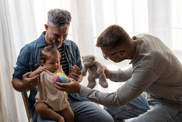 写真 自宅で養子の女の赤ちゃんを持つ男性のゲイのカップル自宅で娘のlgbtq家族と遊ぶ2人のハンサムな父親多様性の概念とlgbtqの家族関係