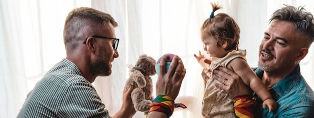 Male gay couple with adopted baby girl at home Two handsome fathers playing with their daughter Lgbtq family at home Diversity concept and LGBTQ family relationship