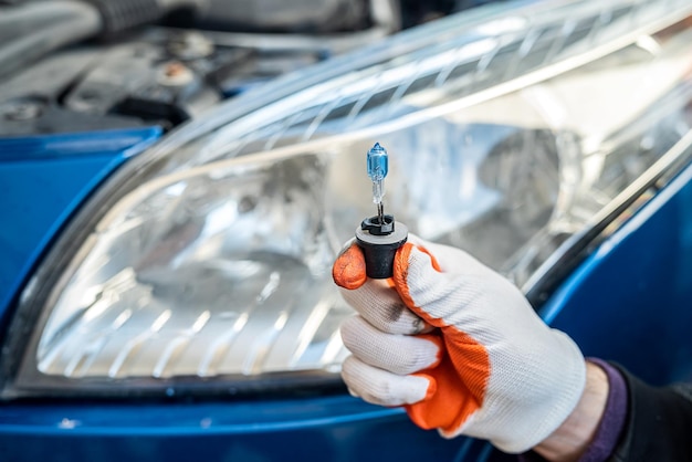 Male gloved hand holds a gelagon lamp on the background of a car headlight. Car repair concept