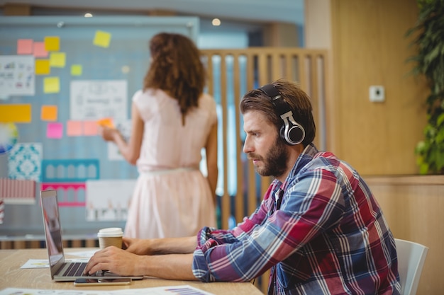 Male graphic designer listening song while using laptop