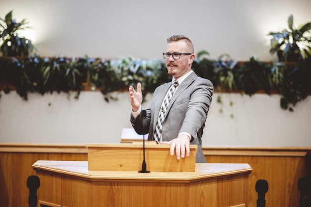 Male in a grey suit preaching words of the Holy Bible at the altar of a church