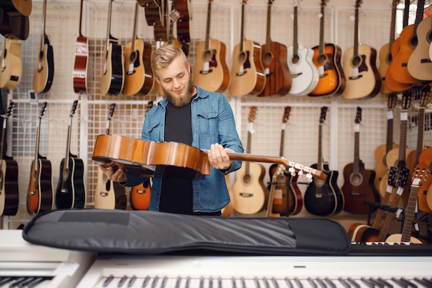 Male guitarist puts acoustic guitar in the case in music store. Assortment in musical instruments shop, musician buying equipment