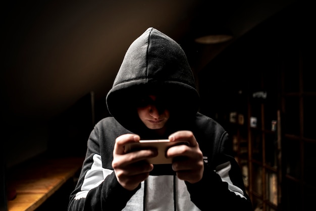 Male hacker in the hood using a mobile phone, stealing your personal data