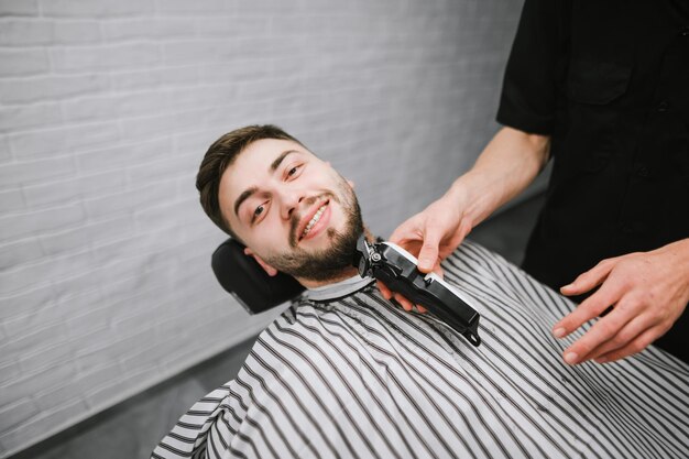 Male hairdresser adjusts the clients beard with a clipper Happy barbershop client