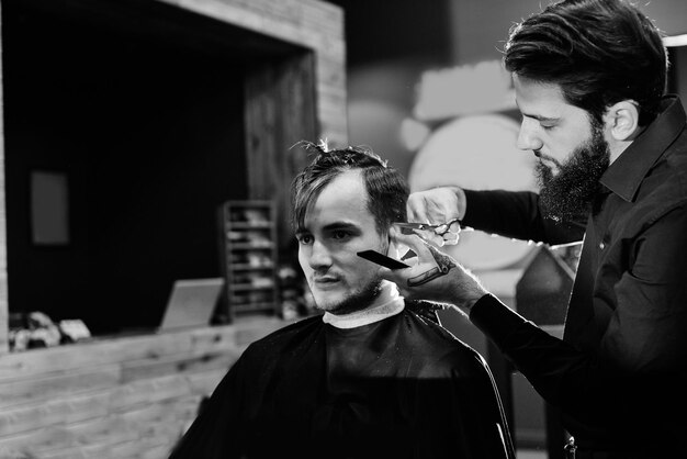 Male hairdresser cuts client with scissors in the barbershop black-and-white photo