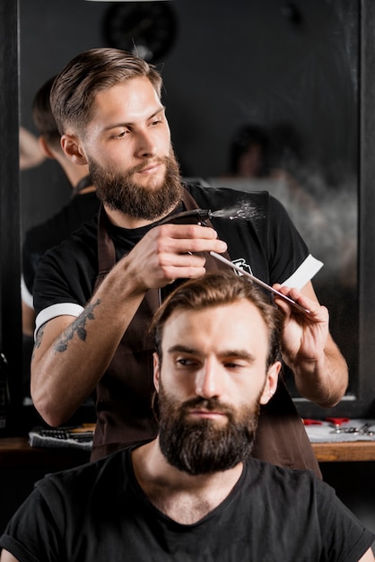 Foto i capelli del cliente maschile di taglio del parrucchiere nel negozio di barbiere