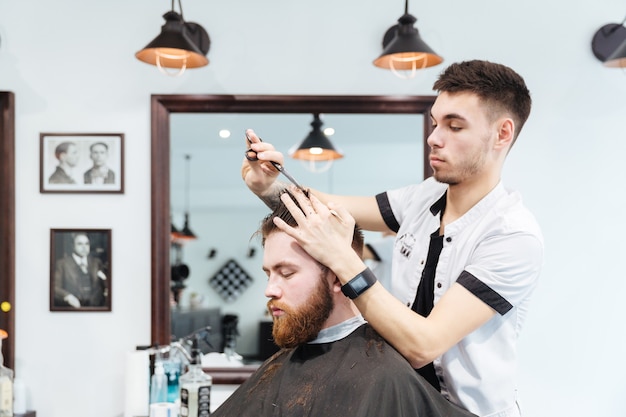 Male hairdresser cutting hair to his client in barbershop