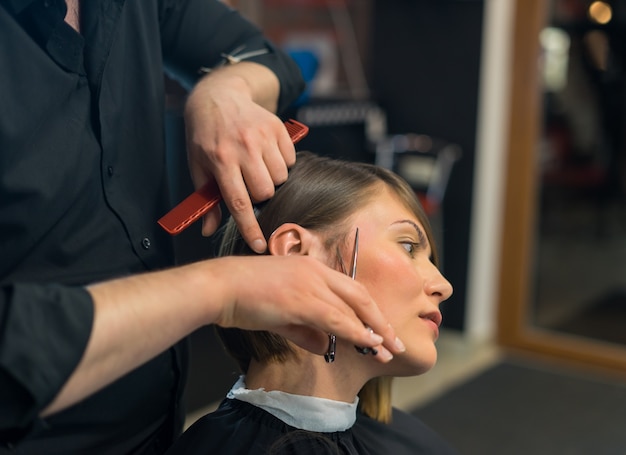 Male hairdresser does a haircut to pretty woman in the beauty salon.