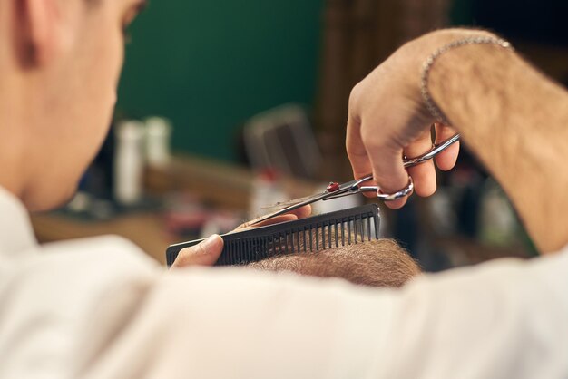 現代の理髪店でクライアントのために短いヘアカットを作る男性の美容師。はさみで伝統的な散髪の概念。