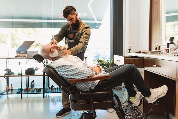 Male hairdresser preparing for shaving senior client in barbershop