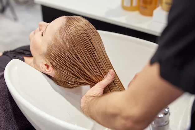 Male hairstylist washing client hair in hairdressing salon