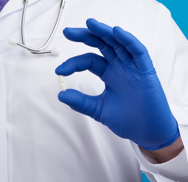 Male hand in blue sterile gloves holds an oval white pill, medical treatment concept for diseases,