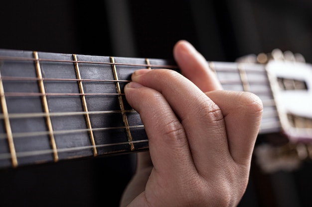 Male hand clamps an acoustic guitar chord.