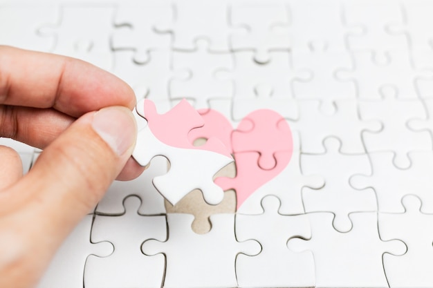 Photo male hand complete a jigsaw puzzle heart ,