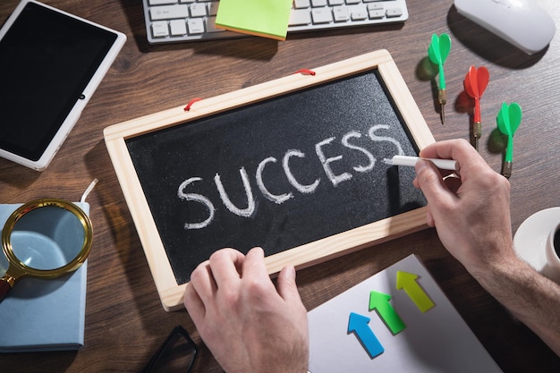 Male hand draws Success text on blackboard with a other objects