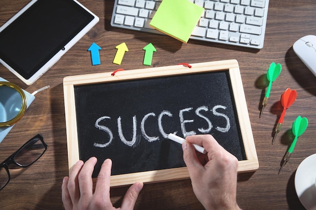 Male hand draws Success text on blackboard with a other objects