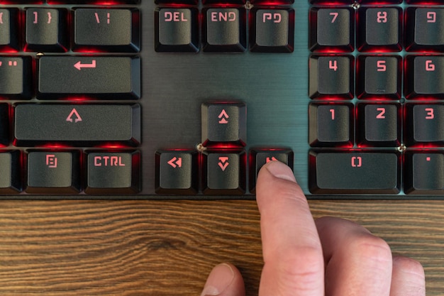 male hand finger presses the arrow to the right on the keyboard lying on a wooden table, close-up