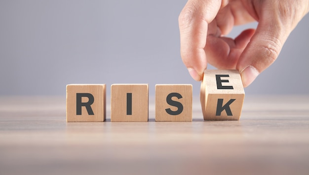 Male hand flipping wooden cube with Risk  to Rise.