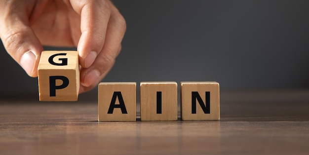 Male hand flips wooden cubes with word Pain to Gain