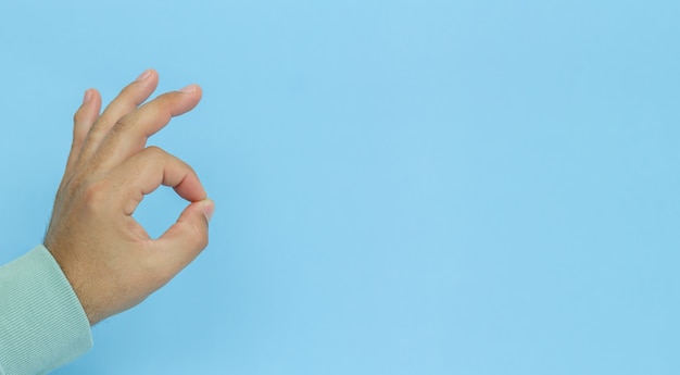 Male hand gesturing OK sign on blue background.