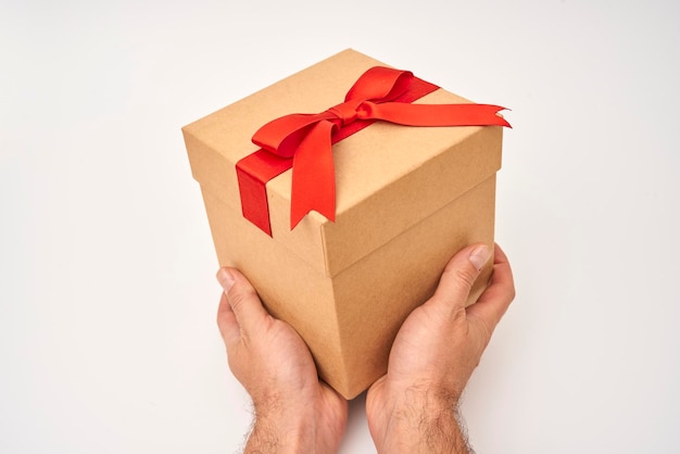 Male hand giving a present box with red ribbon on a white background