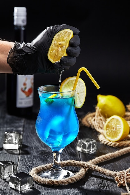 Male hand in glove squeezing lemon into glass with blue lagoon cocktail