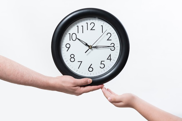 male hand handing a wall clock to boy39s hand