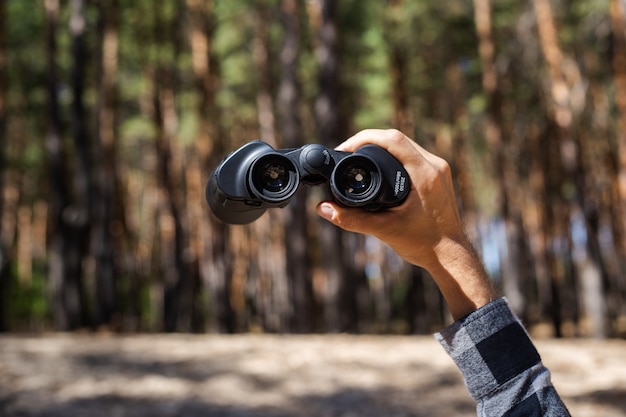 Male hand hold binoculars on the of the forest