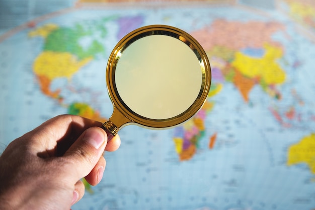 Male hand hold a magnifying glass over the world map.