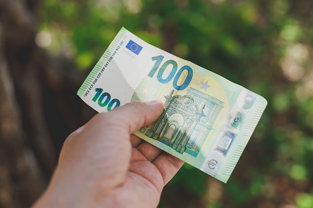 Male hand holding 100 hundredth euro banknote on green wall