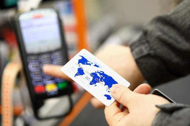 Male hand holding banking card while paying with it at cash desk of supermarket close-up